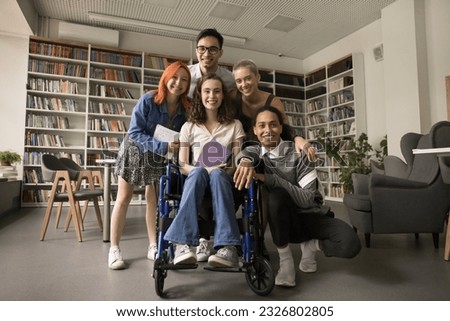 College student friends and classmate girl with disability posing in campus library, standing together, looking at camera, smiling, laughing, promoting inclusive educational environment