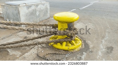 Rusty bollard with knotted mooring rope. Outdoor picture of nautical equipment taken on a vessel.
