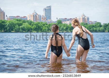 In the summer on the beach, two girls girlfriends play on the banks of the river.