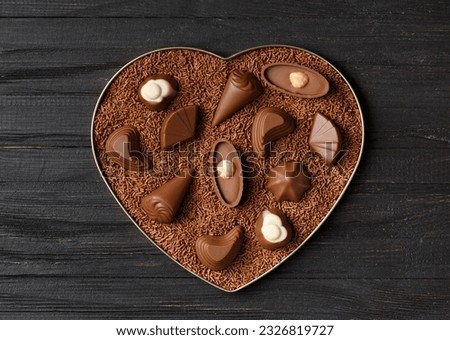 Chocolate candies in chocolate chips in a heart-shaped box on a dark wooden background top view, Valentine's Day.