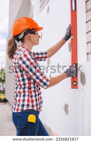 Insulation of the house with polyfoam. The woman worker is checking with the construction level the accuracy of the installation of polystyrene board on the facade.