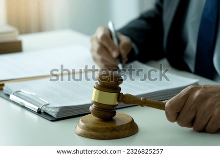 lawyer sitting and holding gavel hands preparing to smash on pedestal symbolizing legal issues and hand holding a pen to write legal documents