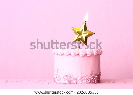 Pink frosted birthday cake with one gold star birthday candle and heart shaped sprinkles against a plain pink background