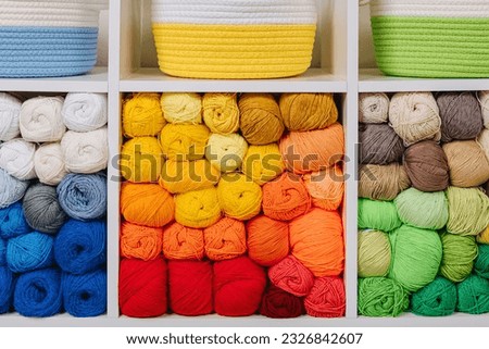 White shelving with colored balls of yarn for knitting. Bright yarn balls lined up on the shelves. Organizing and storage in craft room. Handmade, needle craft, creativity and  hobby.  Royalty-Free Stock Photo #2326842607