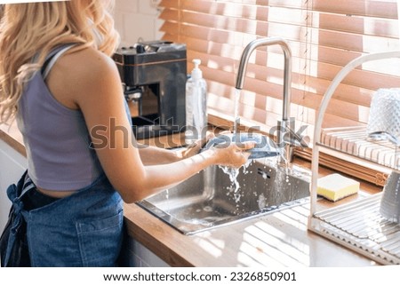 Close up hands of housewife washing dishes in at the kitchen sink. Attractive beautiful woman housekeeper wear apron, cleaning and rinse plate with water for housekeeping housework or chores in house. Royalty-Free Stock Photo #2326850901