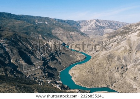 Aerial view of amazing landscape with big mountains and valley with meandering green water river in between hills with motorable roads green agriculture fields under blue sky during summertime