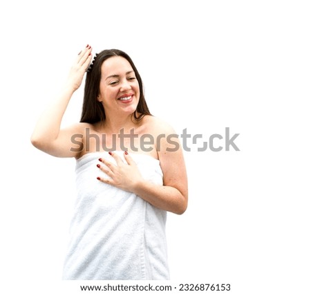 Happy young brunette woman massaging her head while wearing a bathroom towel against a white background