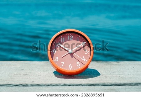 closeup of a pink clock on a weathered wooden pier, next to the water, on a summer day Royalty-Free Stock Photo #2326895651