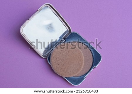 one small open plastic black box with brown powder and a round napkin lies on a pink table