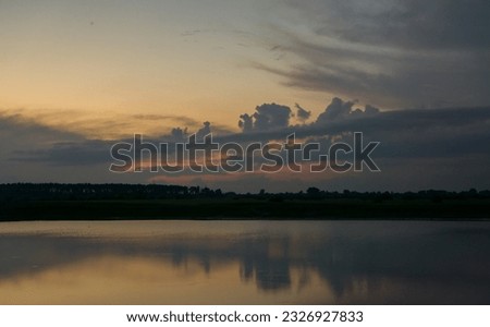 The evening dark sky with clouds illuminated by the setting sun over the dark shore of the reservoir.