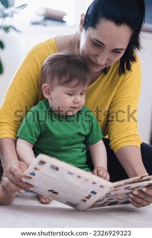 Sweet little boy sitting near loving mother looking at pictures and letters in educational book for children woman helping chubby son developing new skills