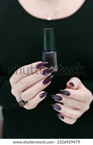 Female hands with long nails and black purple manicure holding a bottle of nail polish