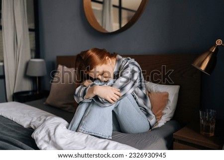 Portrait of sad upset millennial redhead female sitting on bed embrace knees lost in bad pessimistic thoughts suffer alone. Stressed young woman feel lonely desperate has broken heart. Royalty-Free Stock Photo #2326930945