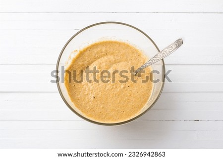 Glass bowl with dough for pumpkin fritters with oatmeal on a white wooden background, top view. Stage of cooking homemade food. Royalty-Free Stock Photo #2326942863