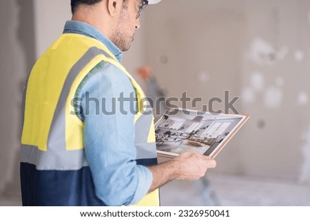 Focused worker holding picture in hands looks at interior design image in Scandinavian style man in professional uniform ready to start renovation process in apartment
