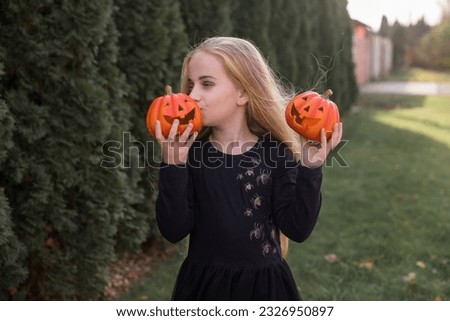 Child in a Halloween costume. A blonde girl with long beautiful hair in a black dress with spiders holds a pumpkin in her hands.