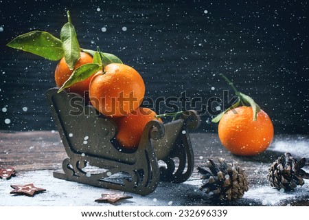 Wooden toy sled with tangerines over wooden background with snow and cone.