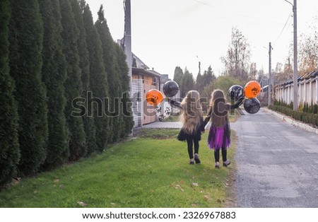 Halloween. Two girls with long beautiful hair, in festive dresses, hold beautiful orange, black and white balloons in their hands.