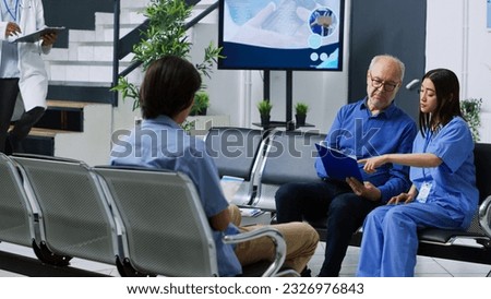Nurse explaining health care treatment to elderly patient during checkup visit consultation in hospital waiting room. Senior man holding clipboard filling medical insurance report. Medicine concept