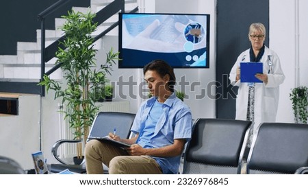 Patient sitting on chiar in hospital lobby, filling medical documents with nurse before attenting examination. Asian young adult signing insurance form during checkup visit. Medicine service