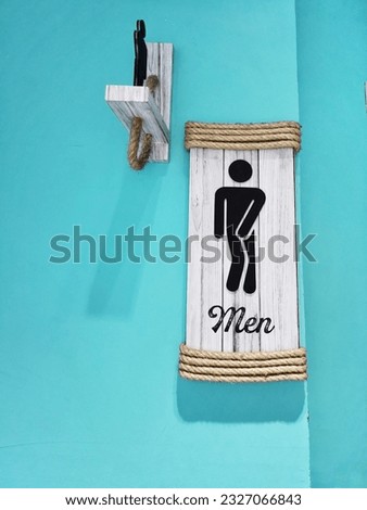 A public restroom sign with a black man on a white wooden background or on a blue wall.  Public toilet or wc sign image with selective focus and copy space on blue.