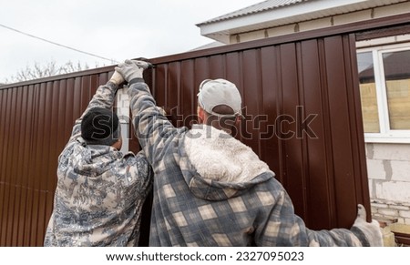 Workers install a metal profile fence.