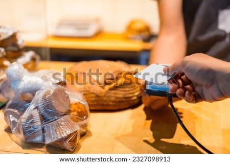 Customer in the bakery shop buying an artisan bread from the baker in the workshop, paying with the card