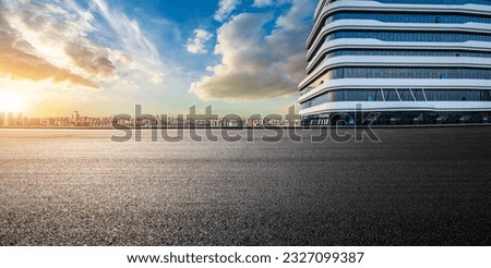 Asphalt road and glass wall with city skyline at sunset
