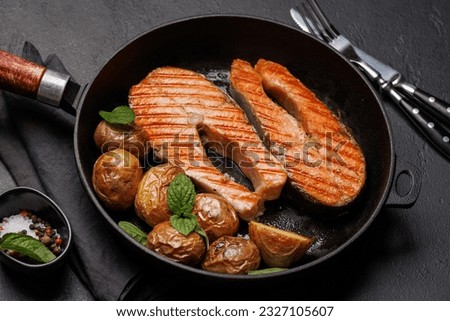 Grilled salmon steaks and potatoes sizzling in a frying pan Royalty-Free Stock Photo #2327105607