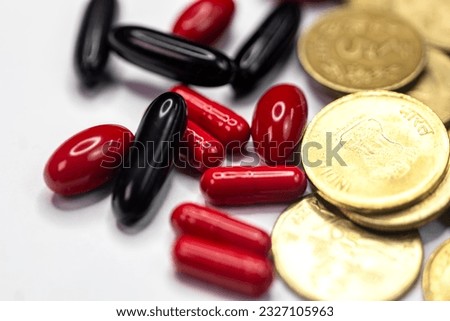 A close-up of Indian 5 rupees coins and red and black pills on a white backdrop. The coins are arranged in a circular pattern, and the pills are scattered around the coins Royalty-Free Stock Photo #2327105963