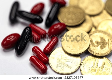 A close-up of Indian 5 rupees coins and red and black pills on a white backdrop Royalty-Free Stock Photo #2327105997