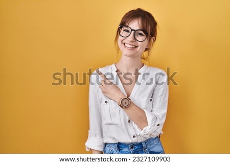 Young beautiful woman wearing casual shirt over yellow background cheerful with a smile on face pointing with hand and finger up to the side with happy and natural expression 