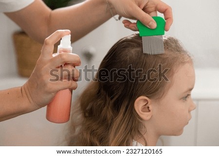 A woman helps to get rid of lice and parasites on the head of a little girl, combs her head with a special comb and and shampoo. Treatment of lice and nits. High quality photo