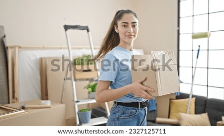 Young beautiful hispanic woman holding package at new home