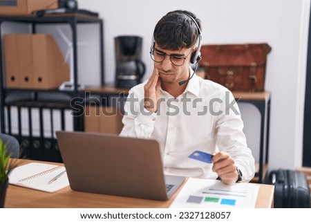 Young hispanic man working using computer laptop holding credit card touching mouth with hand with painful expression because of toothache or dental illness on teeth. dentist concept. 