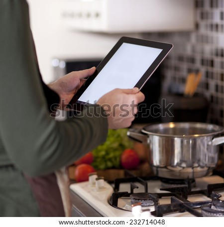 cooking, technology and home concept -man in the kitchen, near the lash, looking at tablet