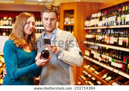 Man taking picture of wine bottle in supermarket with his smartphone