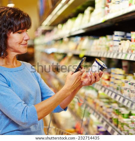 Elderly woman with smartphone scanning barcode of yogurt in a supermarket