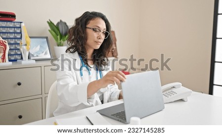 Young beautiful hispanic woman doctor opening laptop working at clinic