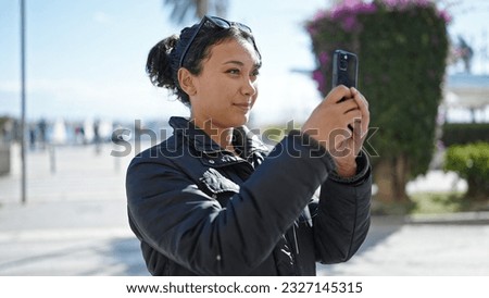 Young beautiful hispanic woman make photo by smartphone at street