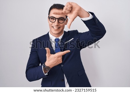 Young hispanic man wearing suit and tie smiling making frame with hands and fingers with happy face. creativity and photography concept. 
