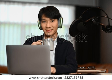 Attractive man using condenser microphone and laptop to recording audio for channel. Radio, podcasts and technology concept