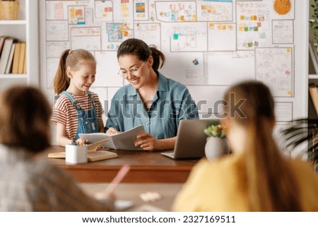 Happy kids and teacher at school. Woman and children are talking in the class. Royalty-Free Stock Photo #2327169511
