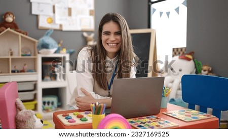 Young beautiful hispanic woman preschool teacher using laptop at kindergarten Royalty-Free Stock Photo #2327169525