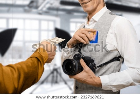 Smiling male photographer with credit card receiving money from client in photo studio, he receives payment from the client, either through a credit card transaction or the physical exchange of cash.
