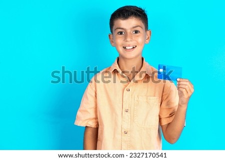 Photo of happy cheerful smiling positive Little hispanic kid boy wearing orange shirt recommend credit card