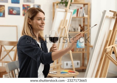 Beautiful woman with glass of wine painting in studio. Creative hobby