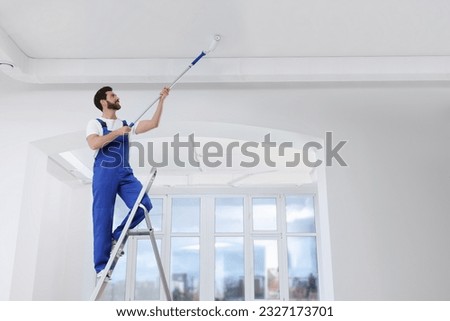 Handyman painting ceiling with roller on step ladder in room Royalty-Free Stock Photo #2327173701