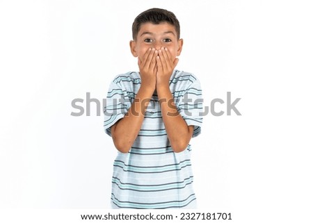 Vivacious Little hispanic kid boy wearing striped T-shirt , giggles joyfully, covers mouth, has natural laughter, hears positive story or funny anecdote
