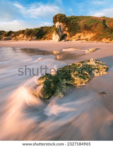 Wave on a mossy rock and sandy beach on Broughton island in Australia